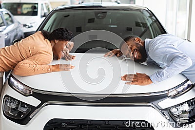 Happy Black Spouses Hugging Hood Of Their New Car In Dealership Office Stock Photo