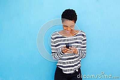 Happy black woman looking at mobile phone by blue background Stock Photo