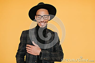 Happy black young man wears elegant dark suit posing with pleased smile. Indoor photo of relaxed mulatto male model in Stock Photo