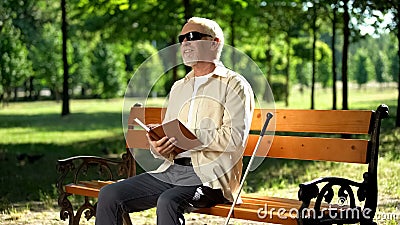 Happy blind pensioner reading funny story in braille book, enjoying rest in park Stock Photo
