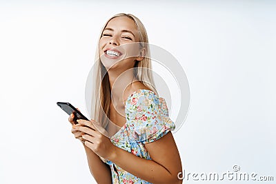Happy blond modern girl, using mobile phone, smiling at camera, standing over white background. Cellular technology Stock Photo