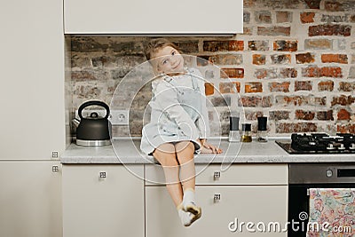 A happy blonde girl with pale skin is posing while sitting on the table in the kitchen Stock Photo