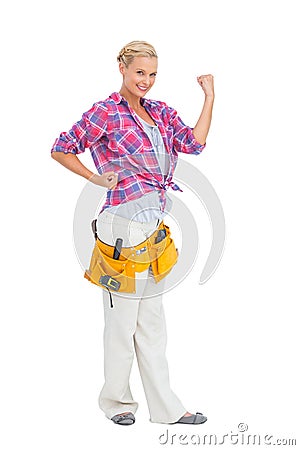 Happy blonde woman tensing arms wearing tool belt Stock Photo