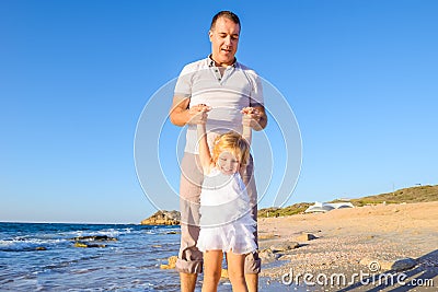 Happy blondy child girl with her father holding hands and having fun walking on the beach. Family vacation, travel concept. Bright Stock Photo