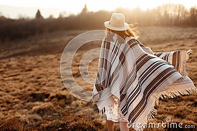 Happy boho woman, walking towards sun, wearing hat and poncho at Stock Photo