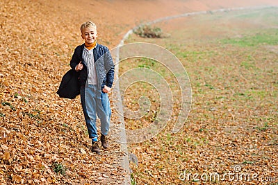 Happy boy with backpack walking in autumn park. Fashion outfit for kid. Autumn boys fashion. Cute kid enjoying fallen leaves. Stock Photo