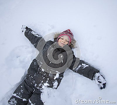 Happy boy lying on snow and making snow angel figure with hands and legs Stock Photo