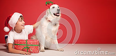 Happy boy posing in Santa Claus hat on red studio background with funny dog. Christmas concept Stock Photo