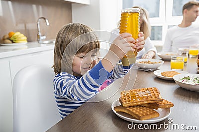 Happy boy pouring honey on waffles while having breakfast with family Stock Photo