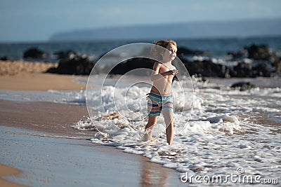 Happy boy running beach near the seaside. Excited amazed kid having fun with running through water in ocean or sea. Stock Photo