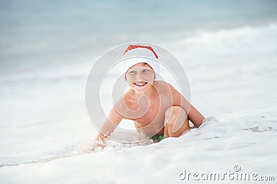 Happy boy in Santa`s hat swims on ocean surfline. Christamas and Stock Photo