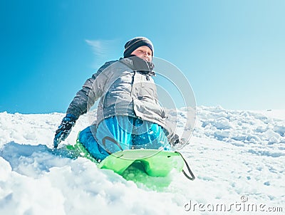 Happy boy slides down from snow hill using the sledge. Winter outdoor activity Stock Photo