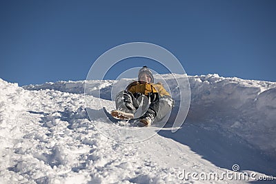 Happy boy sliding down snow hill on sled outdoors in winter, cold season concept Stock Photo