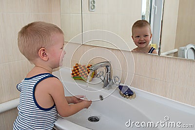 Happy boy taking bath in kitchen sink. Child playing with foam and soap bubbles in sunny bathroom with window. Little baby bathing Stock Photo