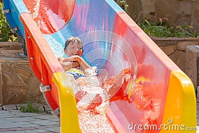 A happy boy on water slide in a swimming pool having fun during summer vacation in a beautiful aqua park. A boy Stock Photo