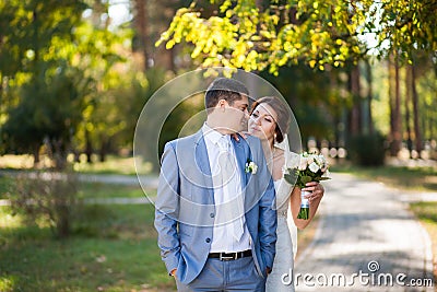 Happy bride, groom standing in green park, kissing, smiling, laughing. lovers in wedding day. happy young couple in love. Stock Photo