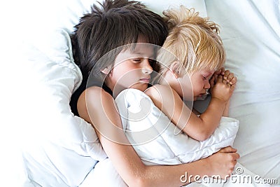 Happy brother with little brother lying in a bed together, kissing and hugging. Siblings. Little brother sleeping and seven years Stock Photo