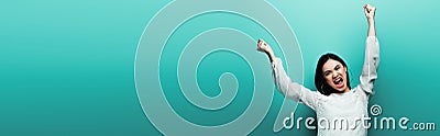 Happy brunette asian woman yelling on turquoise background, panoramic shot Stock Photo