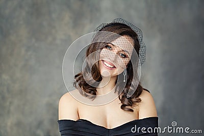 Happy brunette woman with curly hair in black veil smiling on gray background Stock Photo