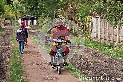 A happy Buddhist monk driving a motorbike on a village street Editorial Stock Photo