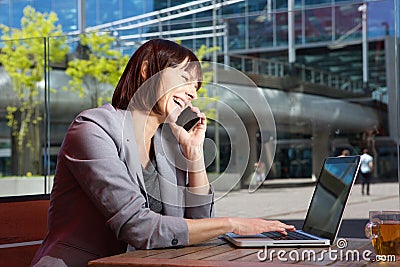 Happy business woman talking on mobile phone while working on laptop Stock Photo