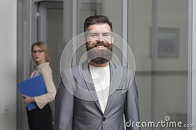 Happy businessman with blurred woman on background. Bearded man in formal suit in office. Confident man smile with beard Stock Photo