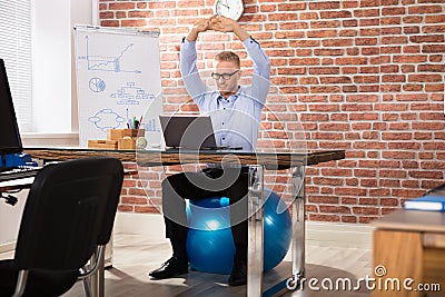 Happy Businessman Relaxing On Fitness Ball In Office Stock Photo