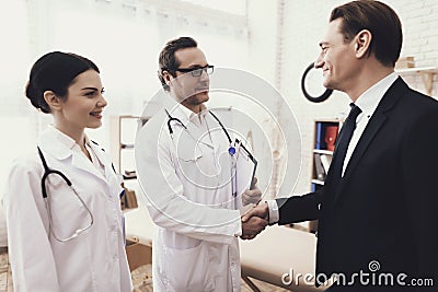 Happy businessman shaking hands with doctor who cured ailment. Acknowledgments. Stock Photo