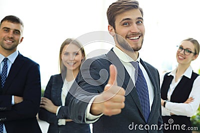 Happy businessman showing his thumb up and smiling while his colleagues standing in the background Stock Photo