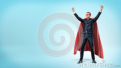 A happy businessman in a superhero red cape standing in victory pose on blue background. Stock Photo