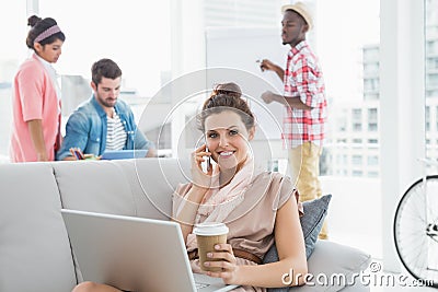 Happy businesswoman phoning and using laptop on couch Stock Photo