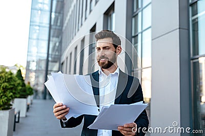 Happy busy handsome young caucasian guy with beard in suit works with documents on street Stock Photo
