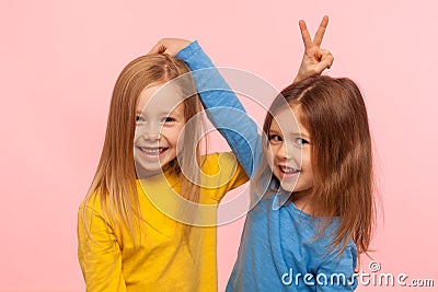 Happy carefree childhood, friendship. Portrait of two positive cute little girls showing bunny ears to each other Stock Photo