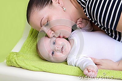 Happy caring mother holding a smiling baby girl and kisses her on changing pad. Stock Photo