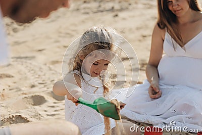 Happy caucasian family in white dress, mother and dad playing with little girl with sand toys playing in sandbox at Stock Photo