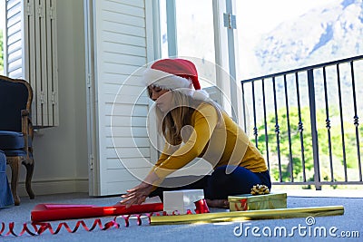 Happy caucasian woman in santa hat sitting on floor and packing gift at christmas at home Stock Photo