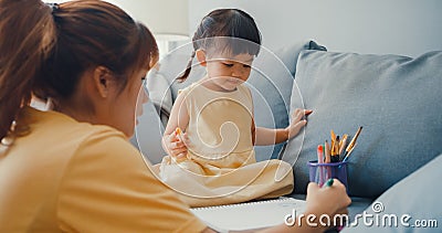 Happy cheerful Asia family mom teach girl paint use album and colourful pencils having fun relax on couch in living room at house Stock Photo