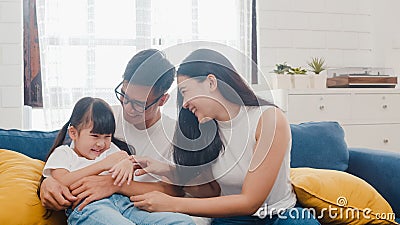 Happy cheerful Asian family dad, mom and daughter having fun cuddling playing on sofa while birthday at house. Self-isolation, Stock Photo
