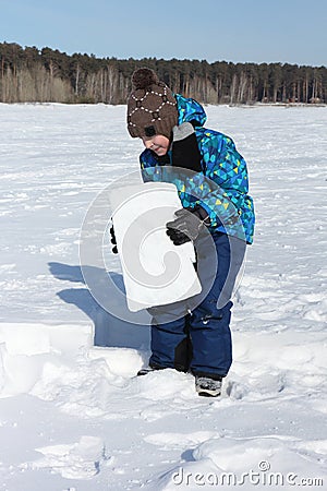 Happy cheerful boy lifting snow block for building an igloo Stock Photo