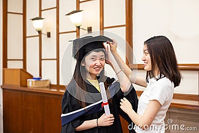 Happy and cheerful Female university graduate students help each other to put on academic dress gown and cap or tam on Stock Photo