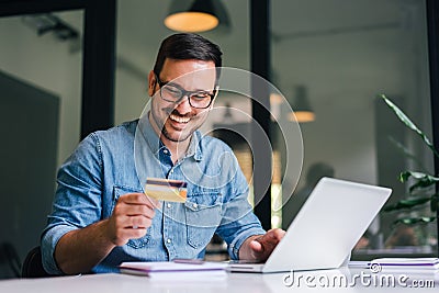 Happy cheerful smiling young adult man doing online shopping or e-shopping satisfied entrepreneur making online payment paying for Stock Photo