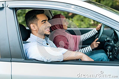 Happy cheerful young muslim woman in hijab is driving car, husband enjoying journey with open window Stock Photo