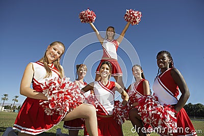 Happy Cheerleaders Holding Pompoms On Field Stock Photo