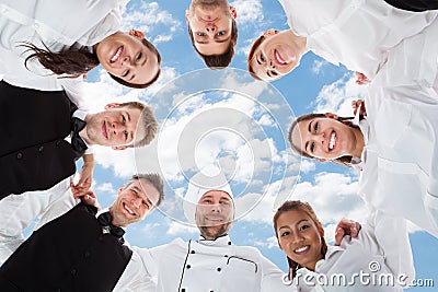 Happy chef and waiters standing in huddle against sky Stock Photo