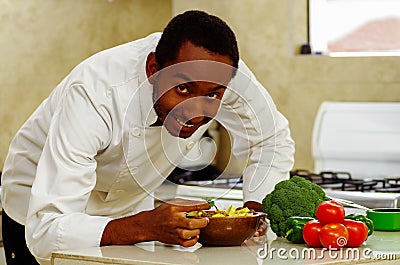 Happy chef wearing white clothes preparing bowl of food in professional kitchen, smiling while finishing last touch Stock Photo