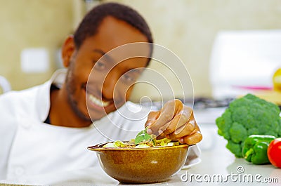 Happy chef wearing white clothes preparing bowl of food in professional kitchen, smiling while finishing last touch Stock Photo