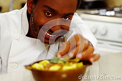 Happy chef wearing white clothes preparing bowl of food in professional kitchen, smiling while finishing last touch Stock Photo