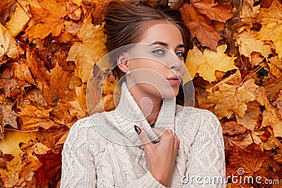 Happy chic pretty young woman with blue eyes with brown hair in a knitted fashionable sweater is resting lying on the orange Stock Photo