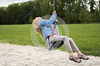 Happy Child blond girl (age 5) rids on Flying Fox play equipment in a children's playground. Stock Photo