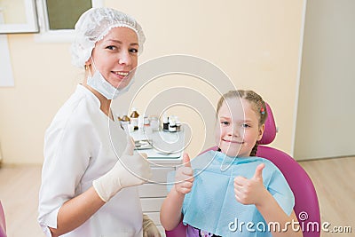 Happy child in dentist chair with female doctor showing thumbs up at dental clinic. Stock Photo